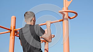 Man doing pull-ups exercises on horizontal bar. Intense workout outdoors. Male with athletic build exercising on bar on street. Ma