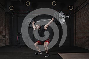 Man doing squats with heavy barbell overhead at gym. Handsome man practicing functional training powerlifting exercises