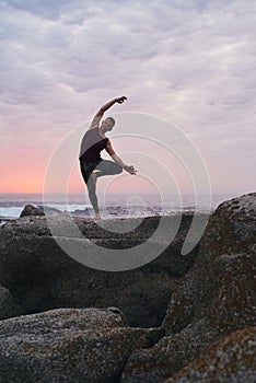 Man doing the tree pose on a rocky coastline