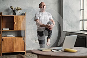 Man doing yoga exercise at home using online lesson on notebook