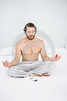 Man doing yoga while listening to music on bed