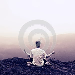 Man is doing Yoga pose on the rocks peak within misty morning