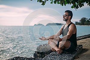 Man doing yoga by the sea. A handsome guy is sitting on the ocean at sunset