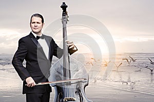 Man with doublebass standing by the ocean