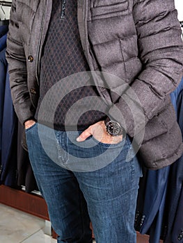 A man in a down jacket and jeans stands in the trading floor of a men`s clothing store, hands in pockets