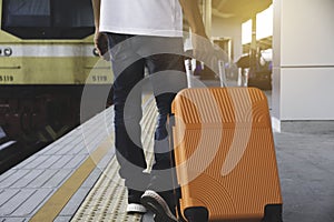 Man dragging orange suitcase luggage bag, walking in train station. Travel concept