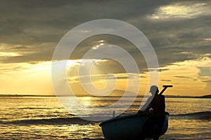 Man drags his fishing boat ashore at sunset
