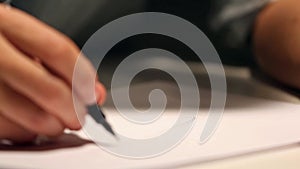 Man is drawing or writing on white sheet of paper. Macro shot of business wearing a shirt and writing on paper behind the desk