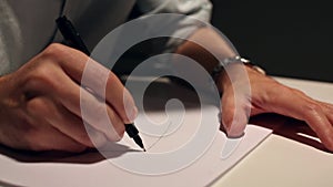 Man is drawing or writing on white sheet of paper. Macro shot of business wearing a shirt and writing on paper behind the desk