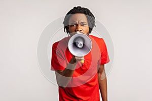 Man with dreadlocks wearing red casual style T-shirt, holding megaphone near mouth loudly speaking, screaming, making announcement