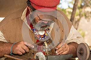 A man dressed as a copper smith from the 1800`s adds detail to a small piece of work with a hammer and awl