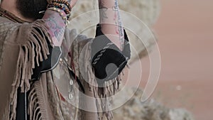 Man dressed as a shaman, standing on a rock in the middle of the desert sands and playing the harmonica