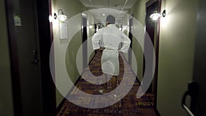 Man dressed in a bathrobe and slippers walking at the long hotel corridor