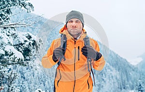 Muž oblečená v žiarivo oranžovej softshellovej bunde s ruksakom má trekking na trase zimných hôr. Aktívni ľudia alebo prežitie v