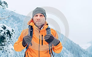 Man dressed bright orange softshell jacket with backpack have trekking on the winter mountains route. Active people or survival in