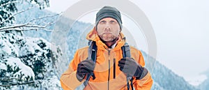 Muž oblečená v žiarivo oranžovej softshellovej bunde s ruksakom má trekking na trase zimných hôr. Aktívni ľudia alebo prežitie v