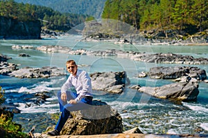 Man dressed business clothes sitting on a rock by the river and mountains