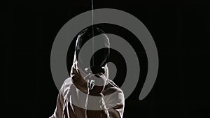 A man dressed for fencing wears a mask and is preparing a rapier. Close-up. Portrait