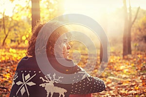 Man dressed in knit sweater with deers sitting on autumn leaves in park.