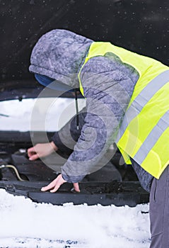 Man dressed in neon green safety vest trying to repair his car.