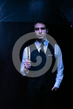 Man dressed in suit holding unbrella and looking at camera at night time