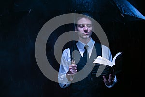 Man dressed in suit holding unbrella and reading book