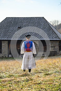 A man dressed in a traditional folk costume. Slovak costume in autumn nature. Old country cottage in the background. Details of