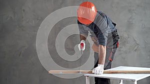 A man dressed in a uniform and an orange hard hat is sawing a piece of block with a hand saw. Copy space.