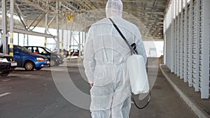 Man dressed white protective overalls walk parking. Disinfectant walking with antiviral liquid tank looking