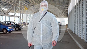 Man dressed white protective overalls walk parking. Disinfectant walking with antiviral liquid tank looking