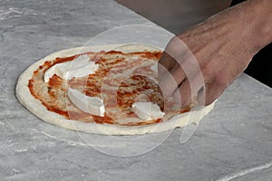 Man dressing a raw pizza with tomato sauce and mozzarella with copy space for your text