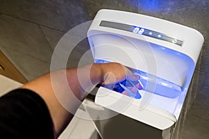 Man dries wet hand in modern vertical hand dryer