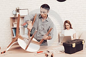 Man with Drill in Hands Repairing Chair in Room.