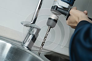 man drilling a hole in a kitchen sink