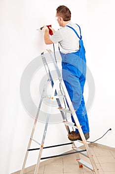 Man drilling hole standing on ladder