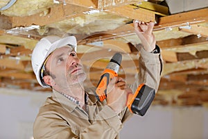 man drilling hole in white ceiling