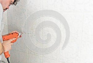 Man drills with an electric drill into the wall of tiles in the bathroom