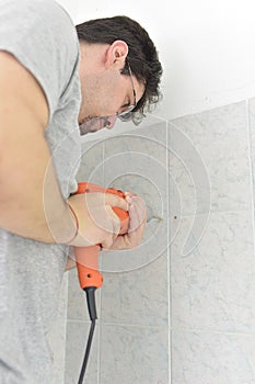 Man drills with an electric drill into the wall of tiles in the bathroom