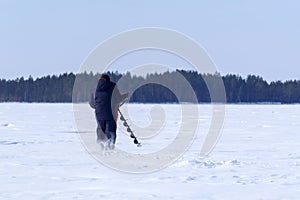 Man drills holes in the ice for ice fishing with an electric auger. selective focus