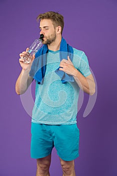 Man drink water after training on violet background. Thirsty sportsman with plastic bottle on purple background. Thirst