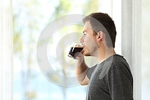Man drinking coffee looking through window