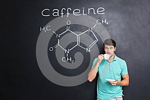 Man drinking coffee over blackboard with structure of caffeine molecule