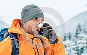 Man drinking a hot drink from thermos flask dressed bright orange softshell jacket while he trekking winter mountains route.