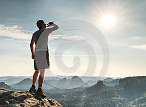 Man drinking water from bottle on rocky summit. Pure nature workout