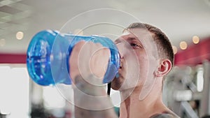 A man is drinking water in the gym with a blue bottle after training.