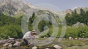 Man drinking water from hands by mountain river while summer hike