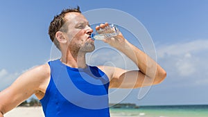 Man drinking water after running at beach. Thirsty sport runner
