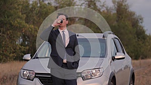 A man drinks cappuccino while looking at the sunset and standing by the car, traveling without being limited in movement