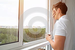 Man drinks cup of coffee on balcony overlooking forest