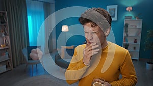 A man drinks water with lemon while standing in the living room close up. The man grabs his jaw, with a pained